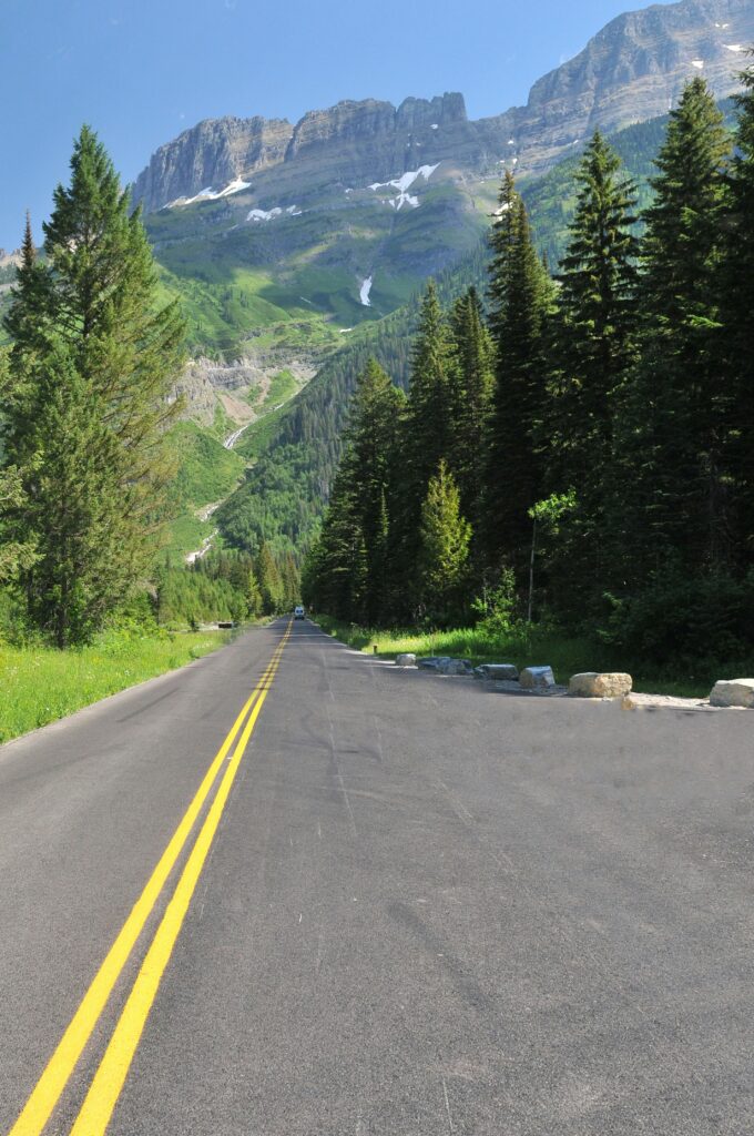Aspen-lined road leading towards majestic mountains under a clear blue sky.
