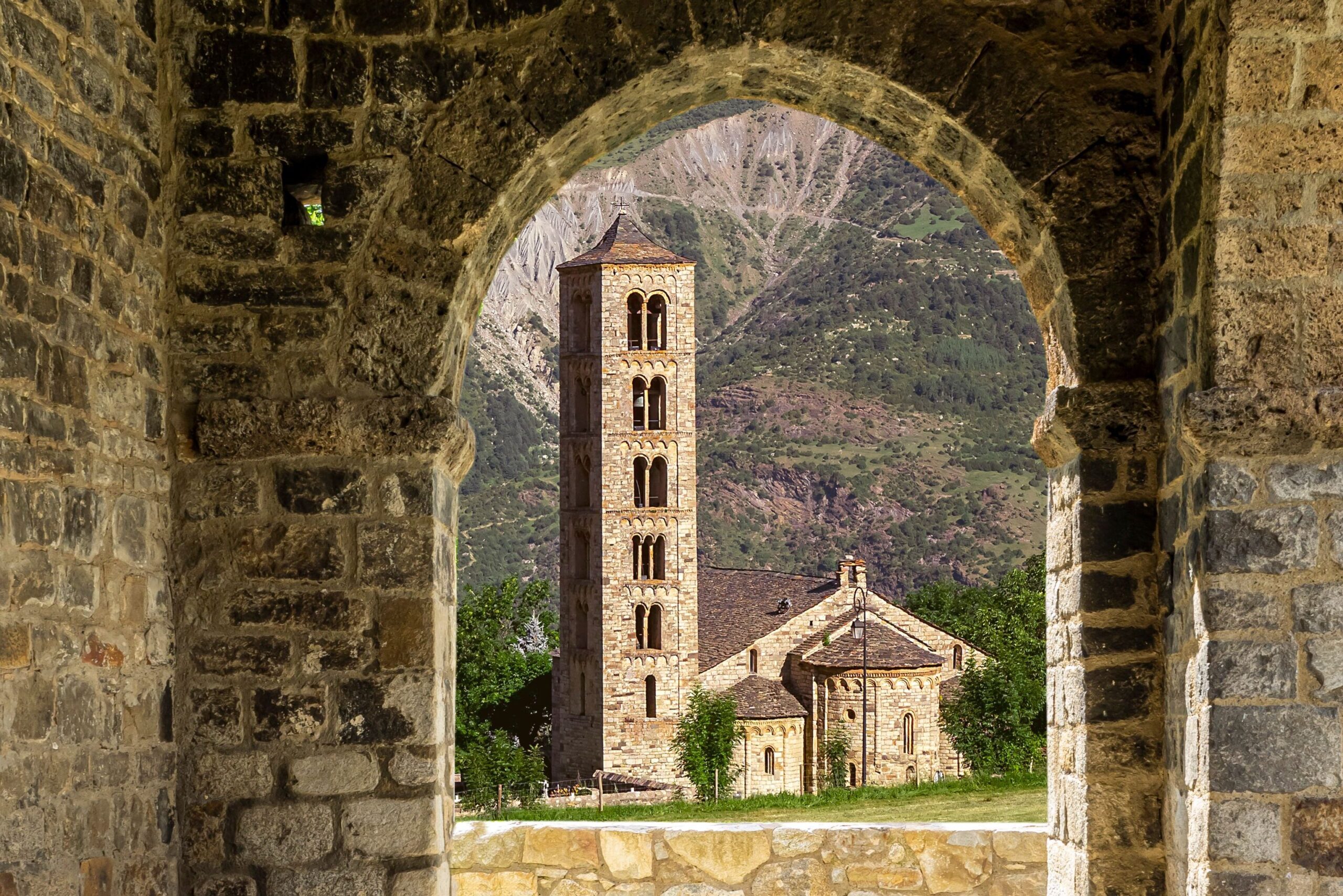 Beautiful view of a Romanesque church and bell tower through stone archway in Bohí, Spain.